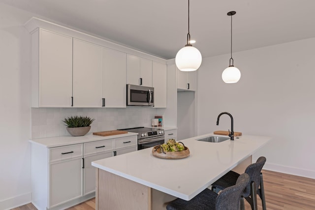 kitchen with stainless steel appliances, white cabinetry, sink, and a center island with sink