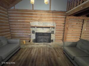 living room featuring a stone fireplace, wood-type flooring, and log walls