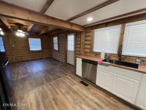 kitchen with log walls, white cabinets, hardwood / wood-style flooring, stainless steel dishwasher, and beam ceiling