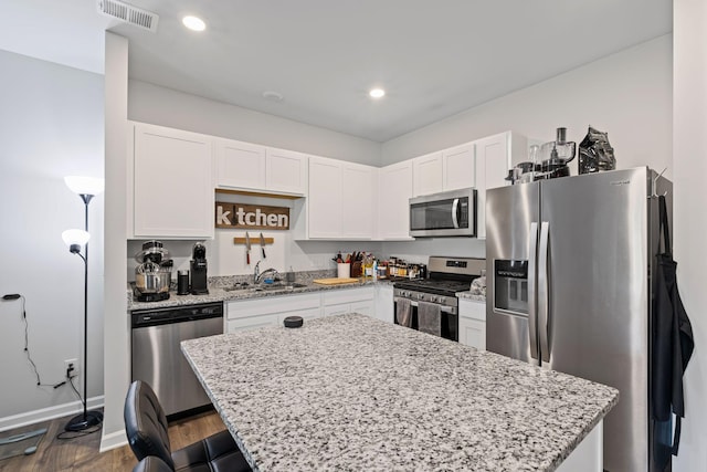 kitchen with sink, white cabinetry, stainless steel appliances, a center island, and light stone countertops