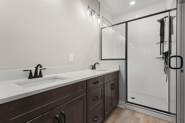 bathroom featuring double vanity, a stall shower, a sink, and wood finished floors