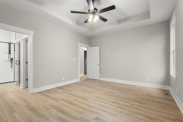 unfurnished bedroom featuring a ceiling fan, a raised ceiling, light wood-style flooring, and baseboards