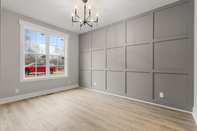 interior space with visible vents, a decorative wall, light wood-style floors, a chandelier, and baseboards