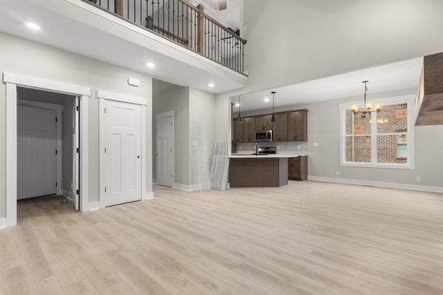 unfurnished living room featuring an inviting chandelier, light wood-style flooring, a high ceiling, and baseboards