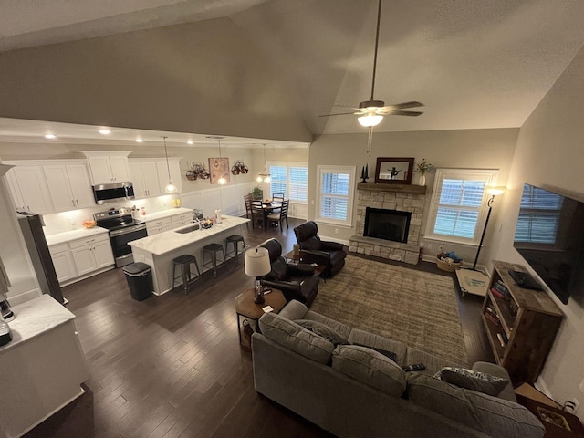 living room with a stone fireplace, dark hardwood / wood-style floors, high vaulted ceiling, sink, and ceiling fan