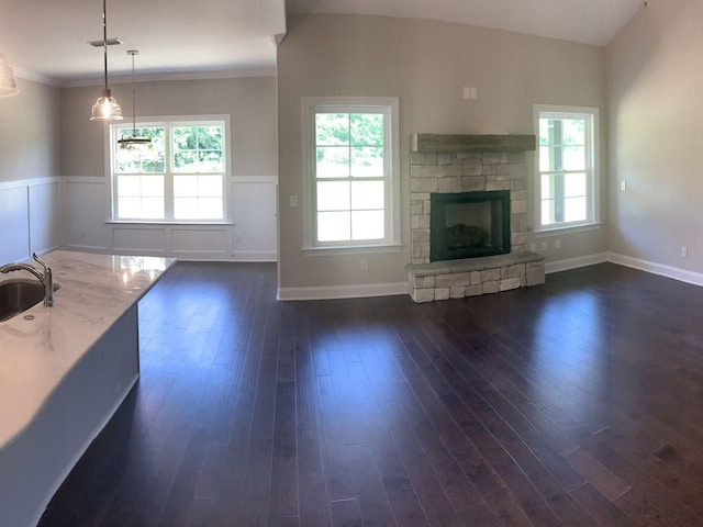 unfurnished living room with plenty of natural light, dark hardwood / wood-style flooring, sink, and a stone fireplace