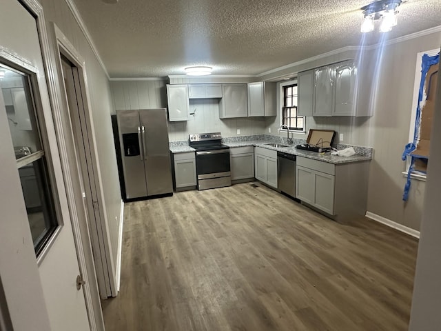 kitchen with appliances with stainless steel finishes, sink, gray cabinetry, ornamental molding, and light wood-type flooring