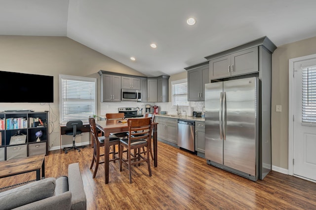 kitchen with lofted ceiling, gray cabinets, stainless steel appliances, dark hardwood / wood-style floors, and tasteful backsplash