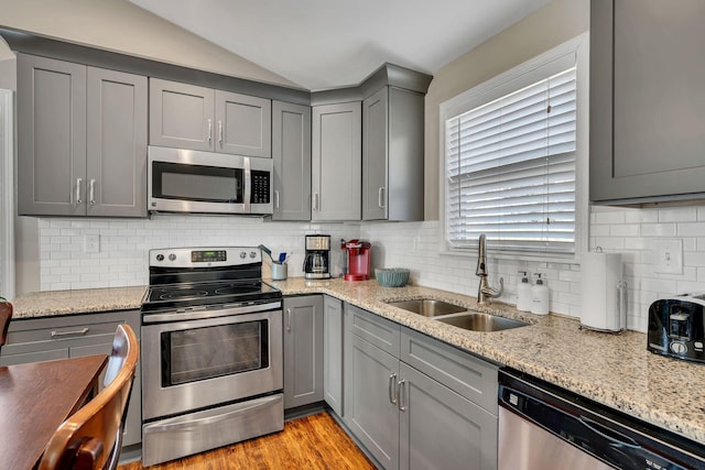 kitchen with appliances with stainless steel finishes, gray cabinets, light stone countertops, and sink