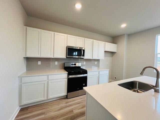 kitchen featuring appliances with stainless steel finishes, tasteful backsplash, sink, white cabinets, and light hardwood / wood-style flooring