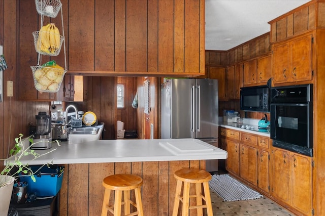 kitchen featuring wooden walls, black appliances, sink, a kitchen bar, and kitchen peninsula