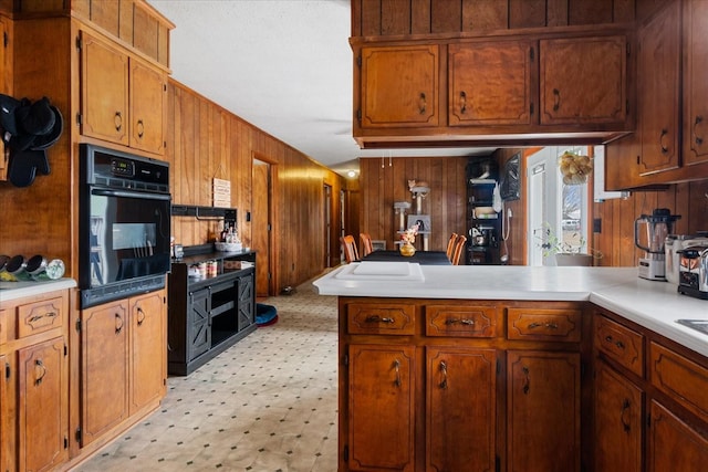 kitchen with black oven, wooden walls, and kitchen peninsula