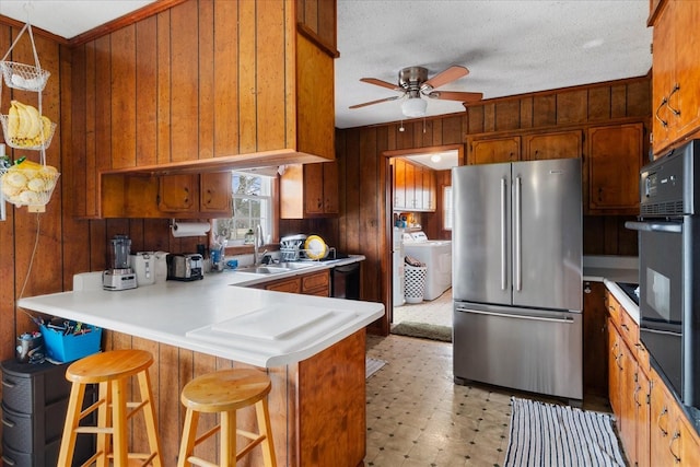 kitchen featuring sink, stainless steel fridge, a kitchen bar, kitchen peninsula, and wood walls