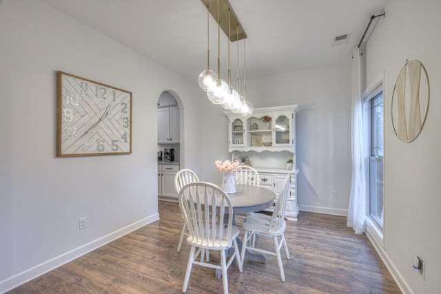 dining area with dark wood-type flooring, arched walkways, visible vents, and baseboards