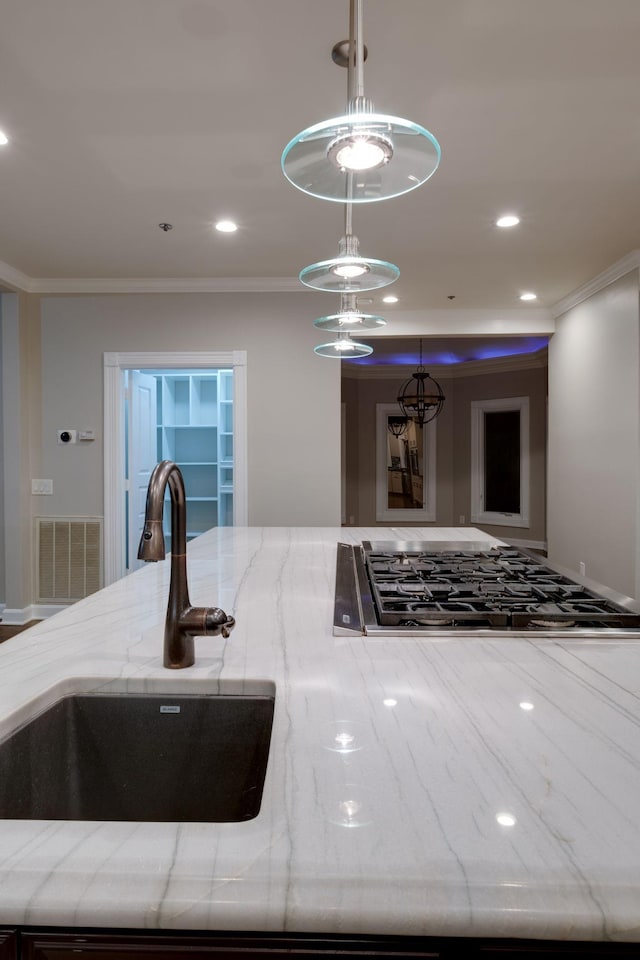 kitchen with cooktop, sink, crown molding, pendant lighting, and light stone countertops