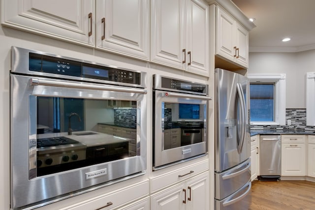 kitchen featuring white cabinets, decorative backsplash, light hardwood / wood-style floors, stainless steel appliances, and crown molding