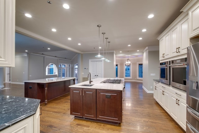 kitchen featuring pendant lighting, sink, stainless steel appliances, dark brown cabinets, and a center island with sink