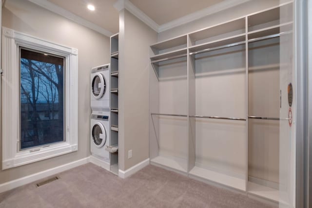 clothes washing area featuring crown molding, stacked washer and dryer, and light carpet