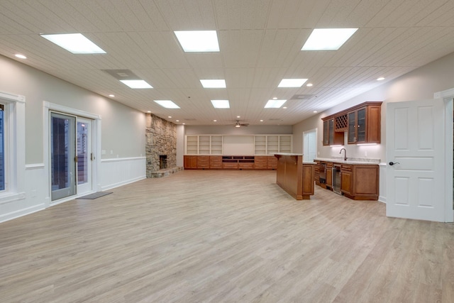 unfurnished living room featuring a stone fireplace, light hardwood / wood-style floors, and wet bar