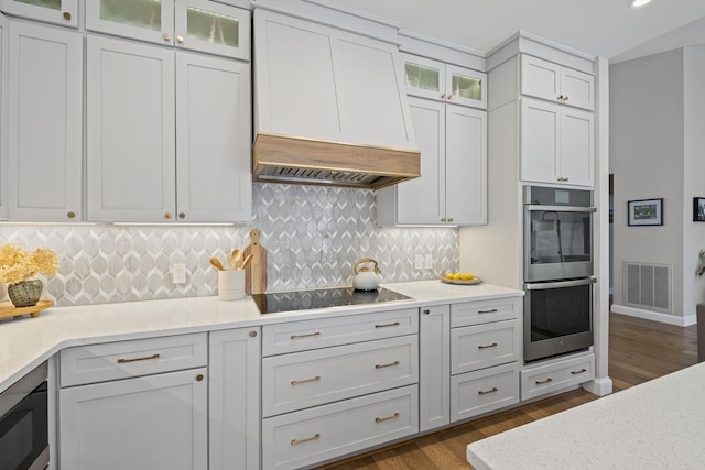 kitchen with white cabinets, backsplash, custom exhaust hood, dark wood-type flooring, and stainless steel double oven