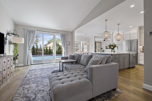 living room featuring lofted ceiling, sink, and light hardwood / wood-style flooring