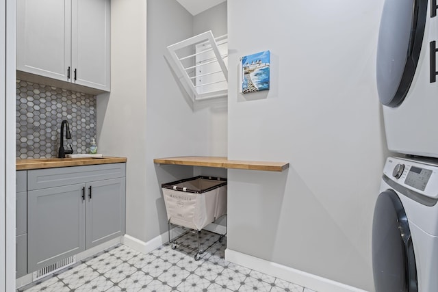 clothes washing area featuring cabinets, stacked washing maching and dryer, and sink