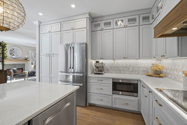 kitchen with stainless steel refrigerator, built in microwave, custom exhaust hood, ornamental molding, and light stone counters