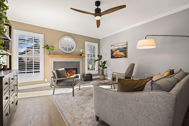 living room featuring crown molding, ceiling fan, a tiled fireplace, and light hardwood / wood-style flooring