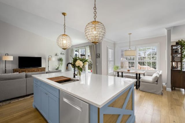 kitchen with decorative light fixtures, sink, stainless steel dishwasher, light hardwood / wood-style floors, and a center island with sink