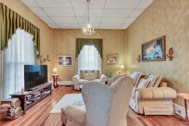 living room with an inviting chandelier, a paneled ceiling, and light wood-type flooring