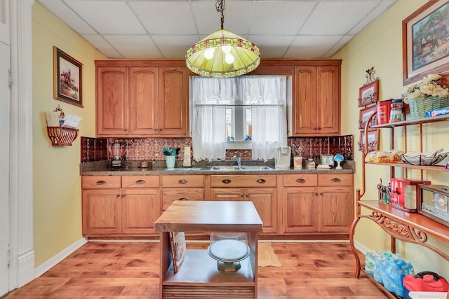 kitchen with sink, decorative backsplash, hanging light fixtures, and light wood-type flooring