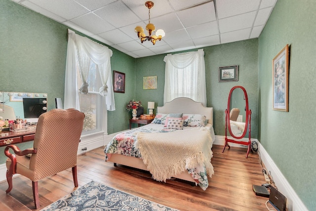 bedroom featuring a drop ceiling, hardwood / wood-style flooring, and an inviting chandelier