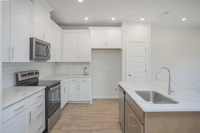 kitchen featuring sink, stainless steel appliances, light stone counters, white cabinets, and a center island with sink