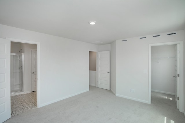 unfurnished bedroom with a closet, ensuite bathroom, a spacious closet, and light carpet