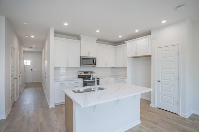 kitchen featuring appliances with stainless steel finishes, light stone counters, an island with sink, white cabinets, and decorative backsplash