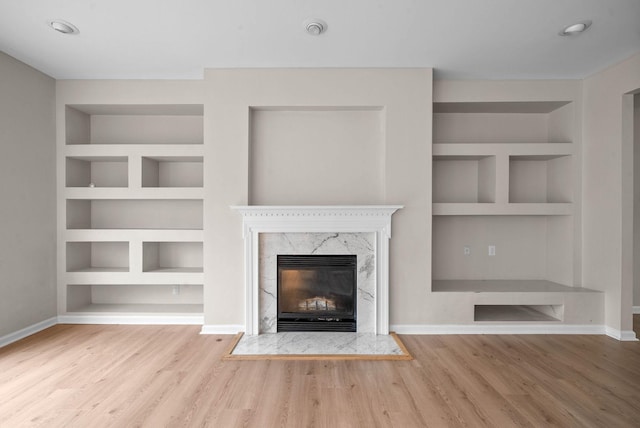 unfurnished living room with hardwood / wood-style floors, built in features, and a premium fireplace