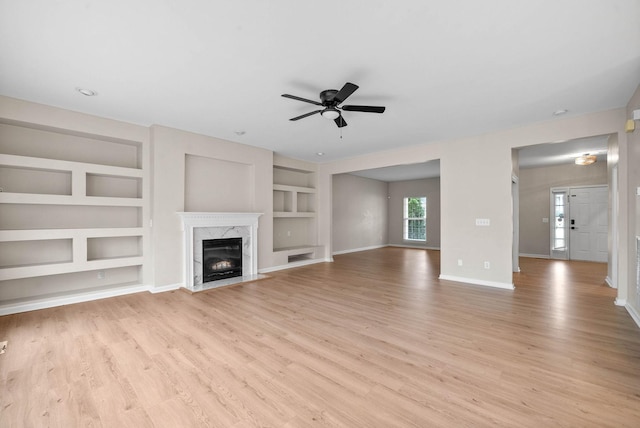 unfurnished living room featuring light hardwood / wood-style flooring, built in features, a premium fireplace, and ceiling fan