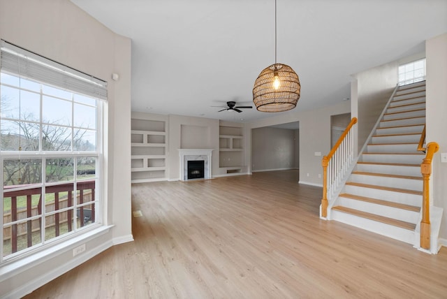 unfurnished living room with a premium fireplace, ceiling fan, built in features, and light wood-type flooring