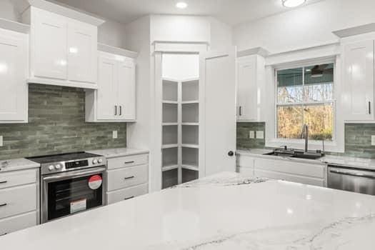 kitchen with light stone counters, decorative backsplash, appliances with stainless steel finishes, white cabinetry, and a sink