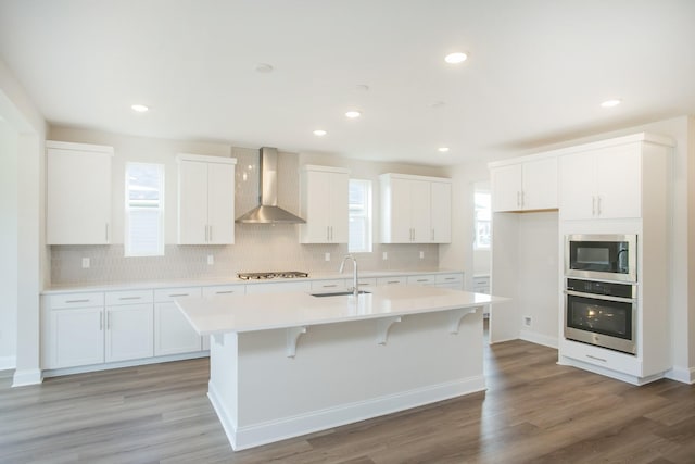 kitchen featuring wall chimney range hood, stainless steel appliances, and white cabinets