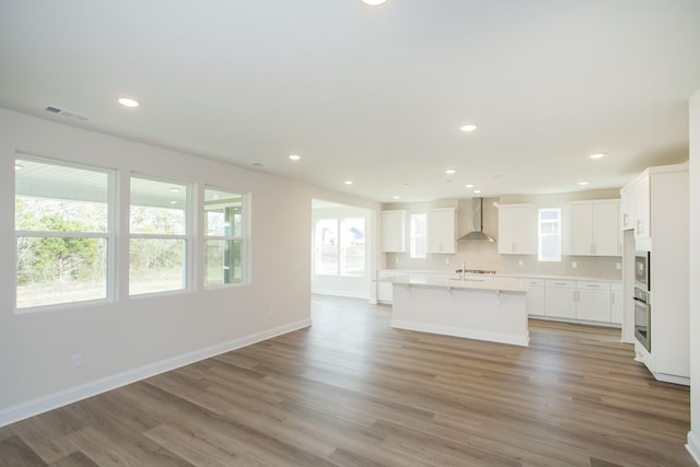 kitchen with white cabinetry, plenty of natural light, a center island with sink, and wall chimney range hood