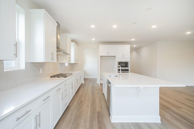 kitchen with white cabinetry, sink, a center island with sink, and wall chimney range hood