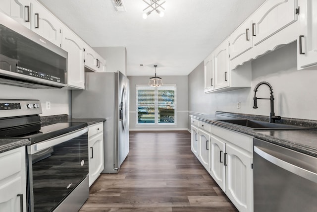 kitchen featuring appliances with stainless steel finishes, decorative light fixtures, sink, white cabinets, and dark wood-type flooring