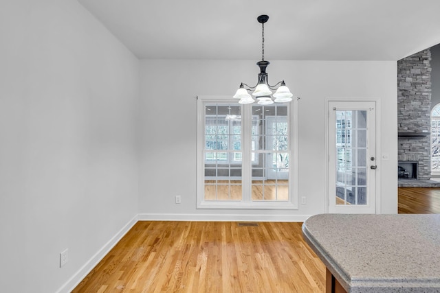 dining space with hardwood / wood-style flooring, plenty of natural light, a stone fireplace, and a notable chandelier