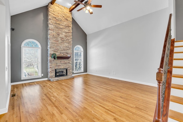 unfurnished living room with light hardwood / wood-style flooring, ceiling fan, beam ceiling, high vaulted ceiling, and a stone fireplace