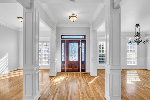 entrance foyer featuring a notable chandelier, ornamental molding, decorative columns, and light wood-type flooring