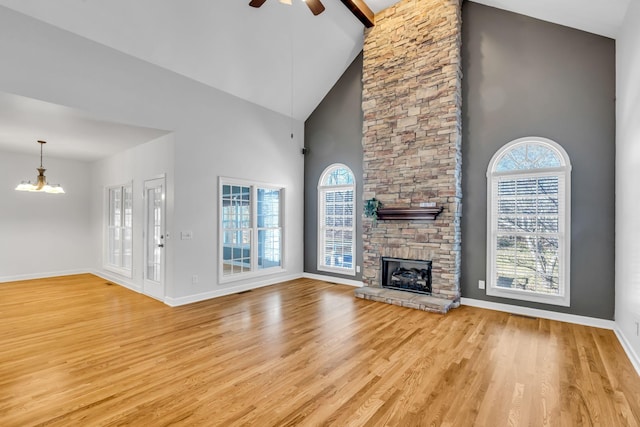 unfurnished living room featuring high vaulted ceiling, light wood-type flooring, ceiling fan with notable chandelier, and a fireplace