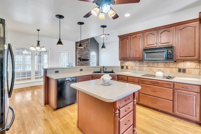 kitchen with sink, light wood-type flooring, a kitchen island, pendant lighting, and black appliances