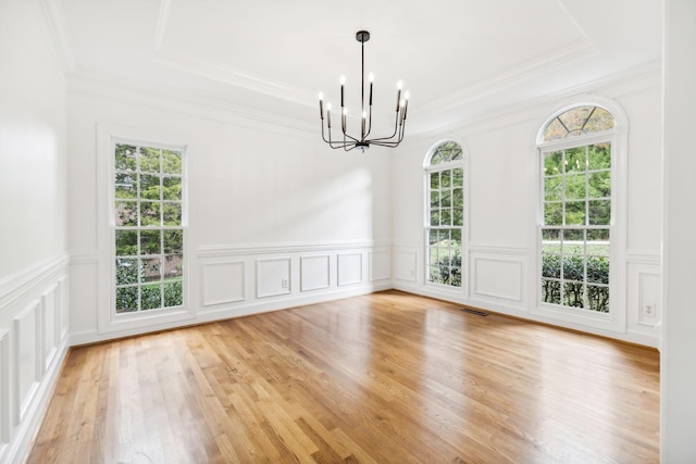 unfurnished dining area featuring crown molding, light hardwood / wood-style flooring, an inviting chandelier, and a tray ceiling