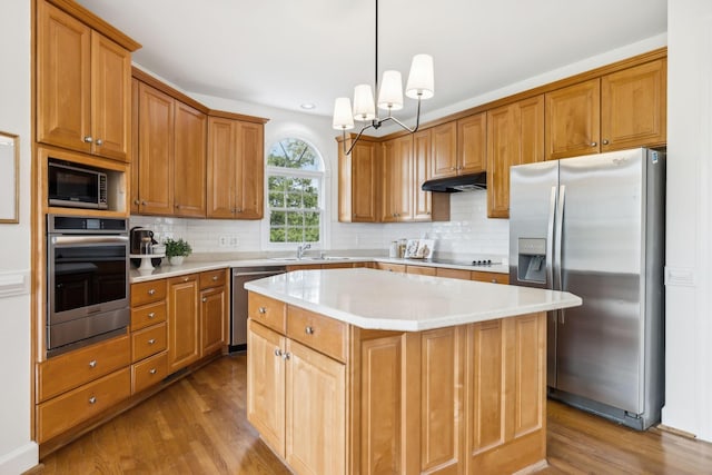 kitchen with tasteful backsplash, a center island, hanging light fixtures, light hardwood / wood-style flooring, and appliances with stainless steel finishes